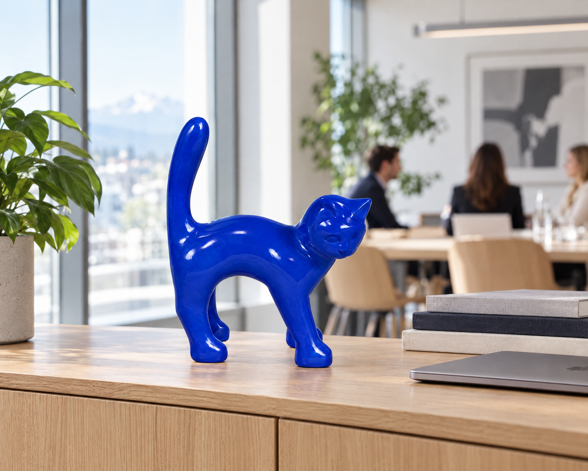 Escultura AlwaysCat azul Klein sobre un aparador de roble en una luminosa oficina suiza, con compañeros reunidos al fondo (puesta en escena digital)